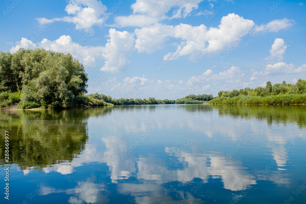 Blue beautiful sky against the background of the river. Clouds are displayed in calm water. On the horizon, the green bank of the Dniester, place for fishing