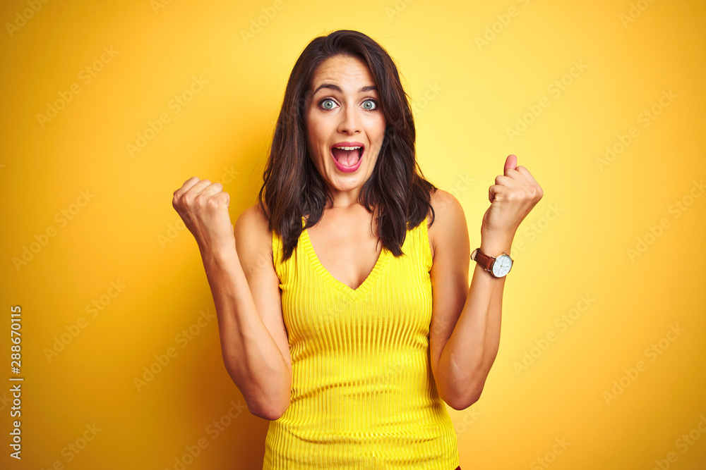 Young beautiful woman wearing t-shirt standing over yellow isolated background celebrating surprised and amazed for success with arms raised and open eyes. Winner concept.