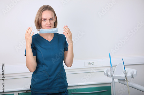 Female dentist doctor puts on a medical mask. Photo in the interior. Koncept of prevention and treatment of teeth.