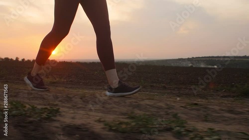 silhouette of young woman legs running on the ground in a field and raising dust, girl in sneakers jogging along a path atsunset, concept of body care and healthy lifestyle photo