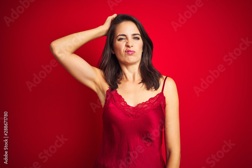 Young beautiful woman wearing sexy lingerie over red isolated background confuse and wonder about question. Uncertain with doubt, thinking with hand on head. Pensive concept.