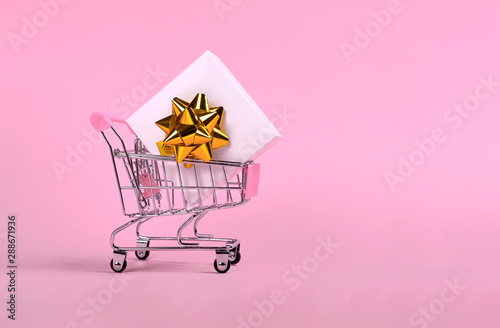 White gift box with bow in shopping cart isolated on pink
