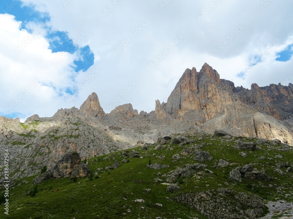The peaks of the Dolomites of the Sassolungo Massif immersed in the clouds and in the nature of Trentino - Alto - Adige, Near the town of Canazei, Italy - August 2019.