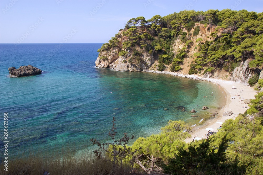 Alonaki beach at summer season with sandy beach and a big rock in the blue sea with swimmers, in a pine trees forest. Background view of the horizon and the sky in the region of Preveza in Greece 
