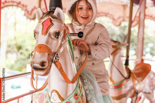 Little girl rides a carousel in an amusement park. Happy child.Focus is shifted to the horse.