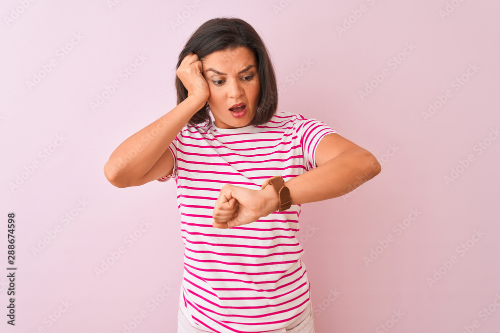 Young beautiful woman wearing striped t-shirt standing over isolated pink background Looking at the watch time worried, afraid of getting late Young beautiful woman wearing striped t-shirt standing over isolated pink background Looking at the watch time worried, afraid of getting late