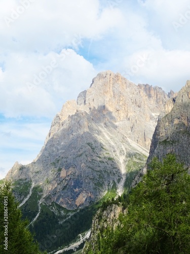 The peaks of the Dolomites of the Sassolungo Massif immersed in the clouds and in the nature of Trentino - Alto - Adige, Near the town of Canazei, Italy - August 2019. © Roberto