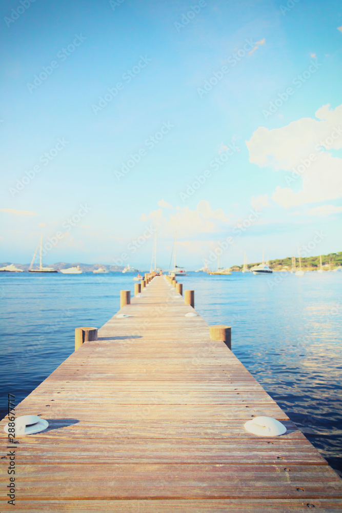 Paysage marin au bout d'un ponton en bois dans la baie des canebiers à Saint Tropez, Vars, Provence, France, eau bleue turquoise et colline à la végétation verte avec des voiliers