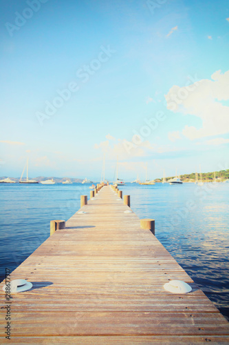 Paysage marin au bout d'un ponton en bois dans la baie des canebiers à Saint Tropez, Vars, Provence, France, eau bleue turquoise et colline à la végétation verte avec des voiliers