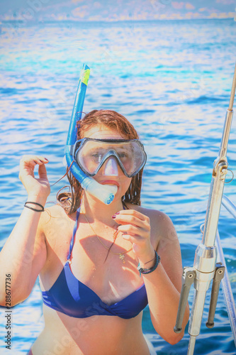 Jeune femme rousse remontant sur son bateau après une plongée avec masque et tuba en pleine mer durant l'été 
