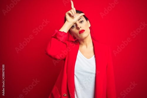 Young beautiful business woman standing over red isolated background making fun of people with fingers on forehead doing loser gesture mocking and insulting.