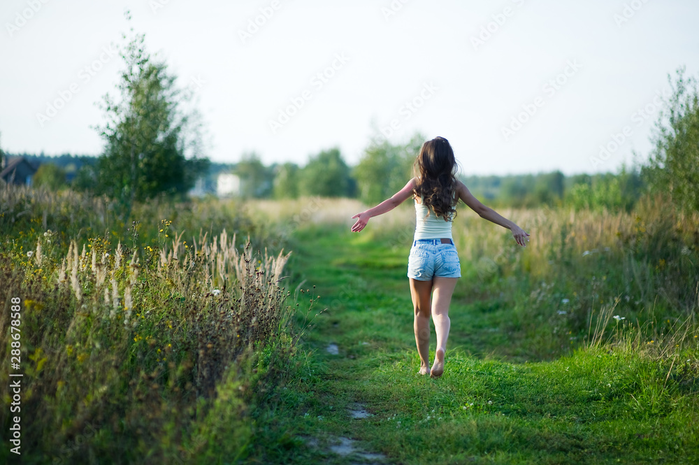 girl in denim shorts with her hair running away barefoot along a country road. copy space girl in denim shorts with her hair running away barefoot along a country road. copy space
