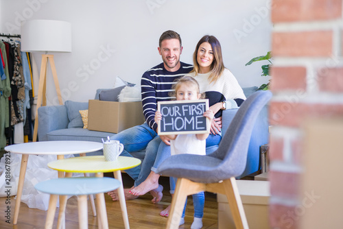 Beautiful famiily with kid sitting on the sofa holding blackboard at new home around cardboard boxes photo