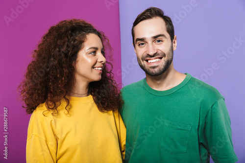 Portrait of cheerful caucasian couple in colorful clothing smiling together, woman looking at man