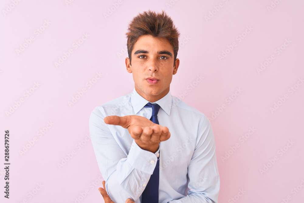 Young handsome businessman wearing shirt and tie standing over isolated pink background looking at the camera blowing a kiss with hand on air being lovely and sexy. Love expression. Young handsome businessman wearing shirt and tie standing over isolated pink background looking at the camera blowing a kiss with hand on air being lovely and sexy. Love expression.