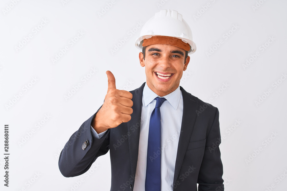 Young handsome architect man wearing suit and helmet over isolated white background doing happy thumbs up gesture with hand. Approving expression looking at the camera showing success.