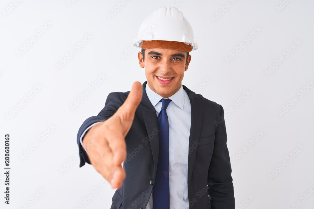 Young handsome architect man wearing suit and helmet over isolated white background smiling friendly offering handshake as greeting and welcoming. Successful business. Young handsome architect man wearing suit and helmet over isolated white background smiling friendly offering handshake as greeting and welcoming. Successful business.
