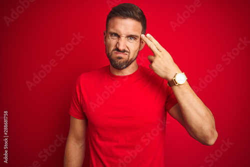 Young handsome man wearing casual t-shirt over red isolated background Shooting and killing oneself pointing hand and fingers to head like gun, suicide gesture.
