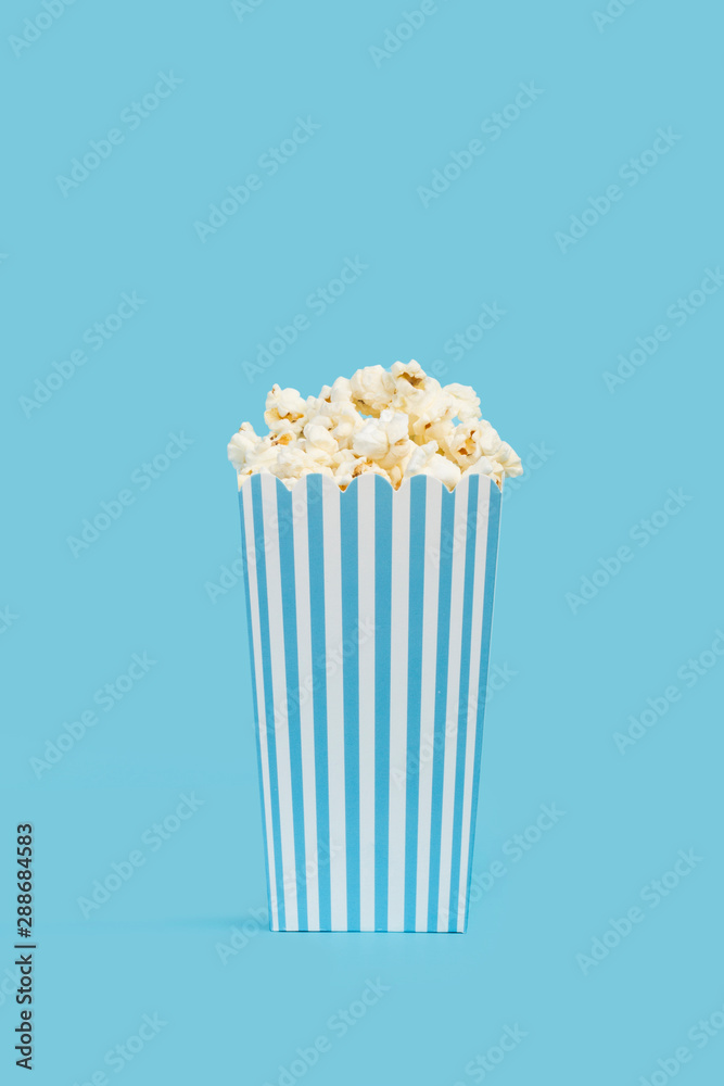 Popcorn palomitas de maíz dentro de una caja de cartón a rayas blancas y celeste sobre fondo un celeste liso y aislado. Vista de frente y de cerca. Copy space. Formato vertical