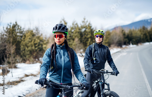 Two mountain bikers resting on road outdoors in winter.
