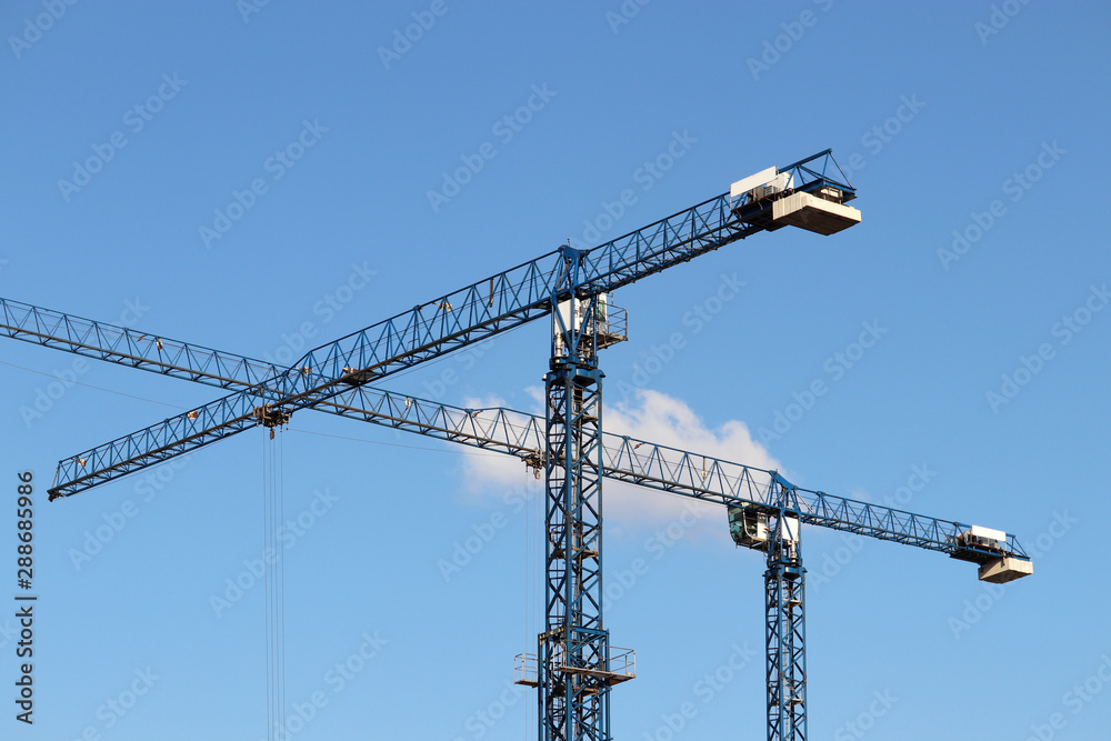 Two construction cranes on clear blue sky background. Concept of housing construction Two construction cranes on clear blue sky background. Concept of housing construction