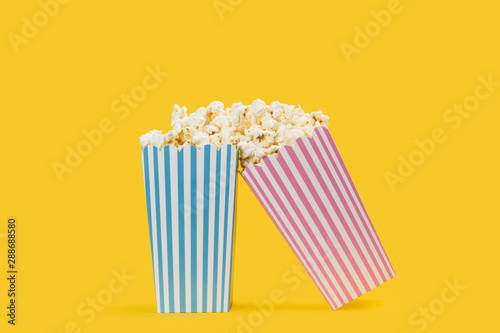Popcorn palomitas de maíz en cajas celeste y rosa a rayas sobre un fondo amarillo brillante y aislado. Vista de frente y de cerca. Copy space © Mercedes Fittipaldi