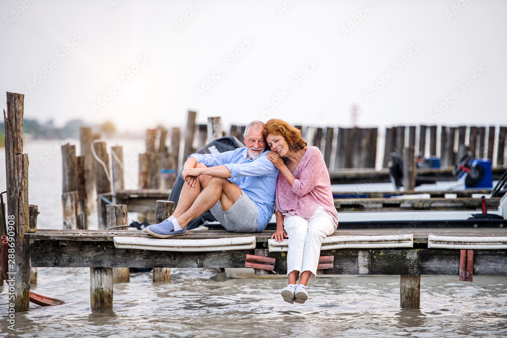 Senior couple on a holiday sitting by the lake, hugging.