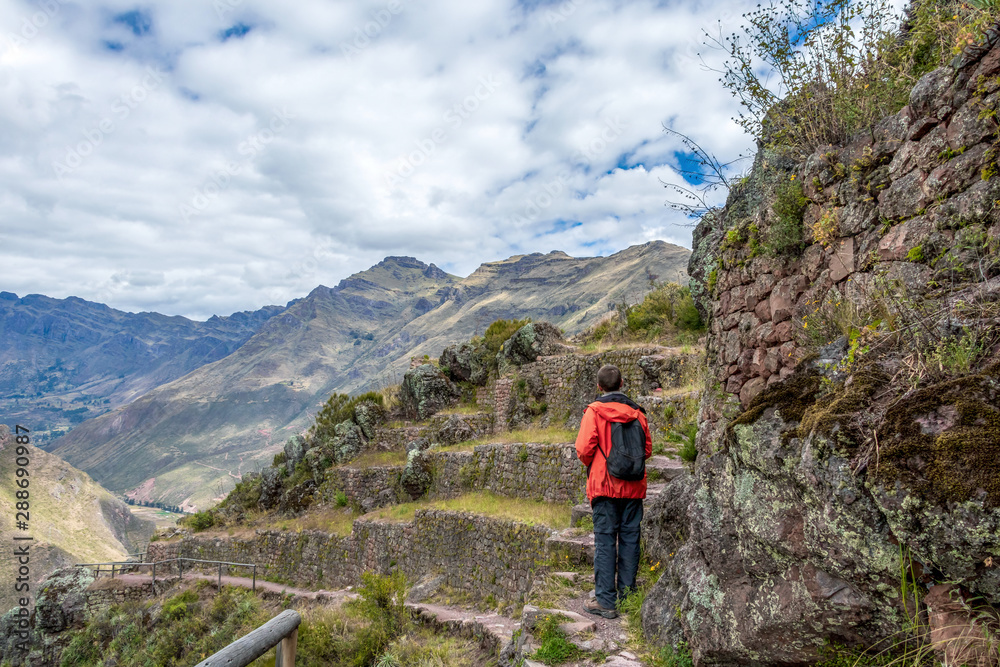 Young male tourist traveling alone in Sacred valley. Solo man hiker with backpack sightseeing inca ruins in Cusco region, Peru