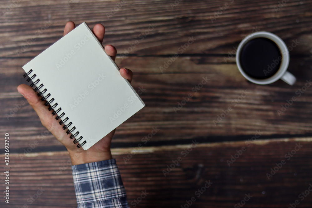 A business man is holding a notebook at wooden table.