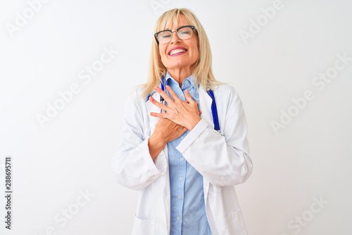 Middle age doctor woman wearing glasses and stethoscope over isolated white background smiling with hands on chest with closed eyes and grateful gesture on face. Health concept.