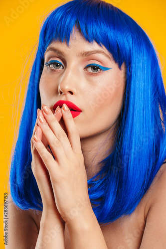 Portrait closeup of sexual woman wearing blue wig looking at camera and holding hands near her mouth