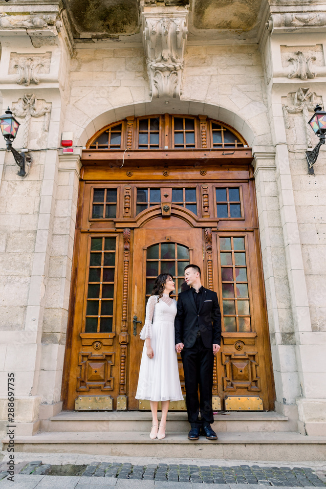 Beautiful Chinese couple posing near antique brown door of old historical building in old European city