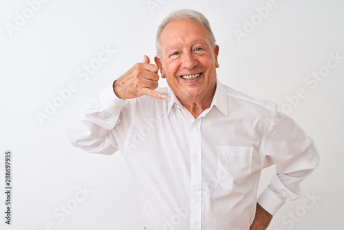 Senior grey-haired man wearing elegant shirt standing over isolated white background smiling doing phone gesture with hand and fingers like talking on the telephone. Communicating concepts.