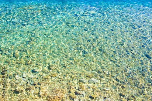 Clear amazing azure coloured sea water. Transparent sea water with sunlight on pebbles. Sea water background.