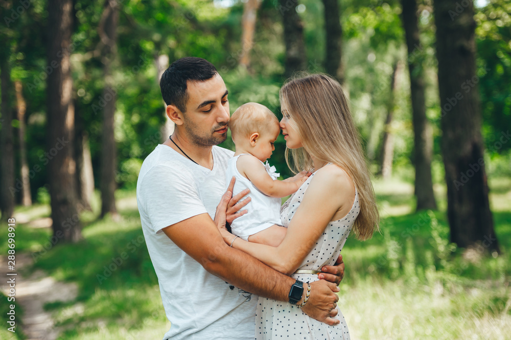 Mom, dad and girl toddler embraces in the summer park. Happy young family spending time together, outside, outdoors. Mom, dad and girl toddler embraces in the summer park. Happy young family spending time together, outside, outdoors.