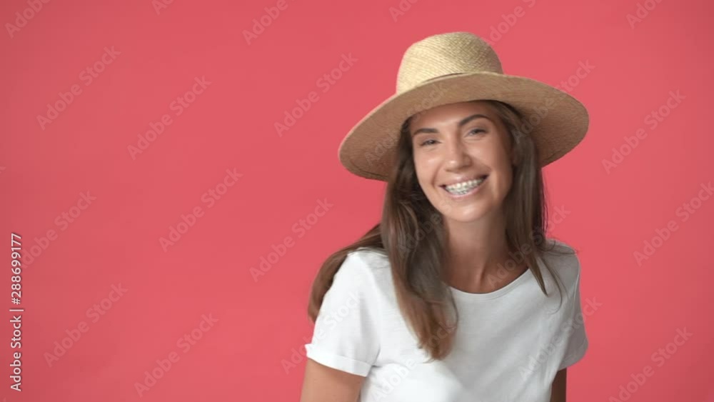 Silly pretty brunette woman in straw hat, white t-shirt standing backwards and turning camera, smiling carefree, enjoying vacation, travelling europe, wearing braces, standing red background Silly pretty brunette woman in straw hat, white t-shirt standing backwards and turning camera, smiling carefree, enjoying vacation, travelling europe, wearing braces, standing red background