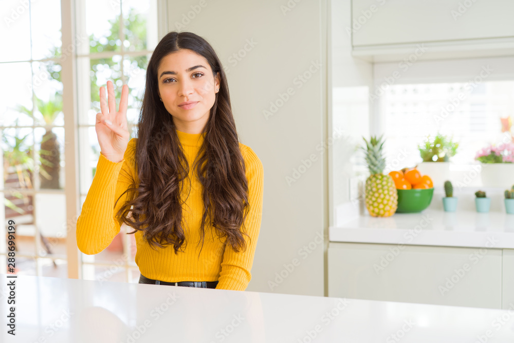 Young beautiful woman at home on white table showing and pointing up with fingers number three while smiling confident and happy. Young beautiful woman at home on white table showing and pointing up with fingers number three while smiling confident and happy.