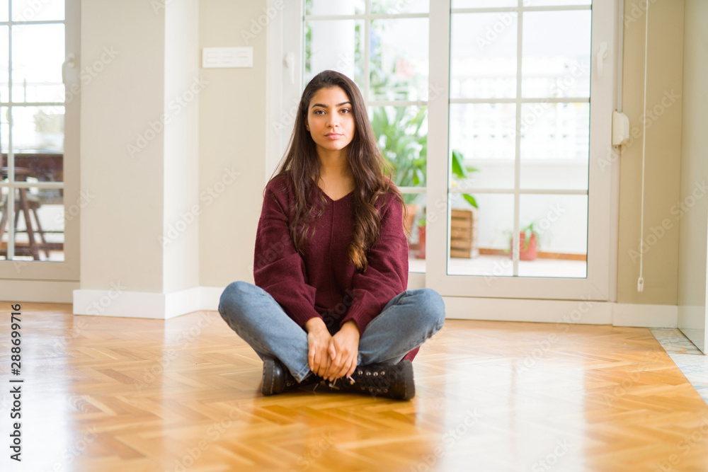 Young beautiful woman sitting on the floor at home with serious expression on face. Simple and natural looking at the camera. Young beautiful woman sitting on the floor at home with serious expression on face. Simple and natural looking at the camera.