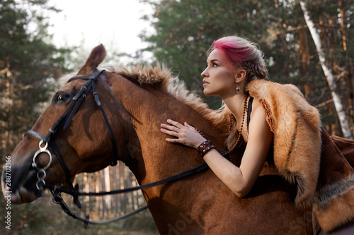 Woman walking with horse autumn on nature. Creative hot pink makeup girl face, hair coloring. Portrait of a girl with a horse. Horse riding in the autumn forest. Autumn clothes and bright red makeup