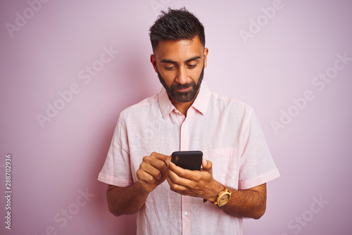 Young indian man using smartphone standing over isolated pink background with a confident expression on smart face thinking serious © Krakenimages.com
