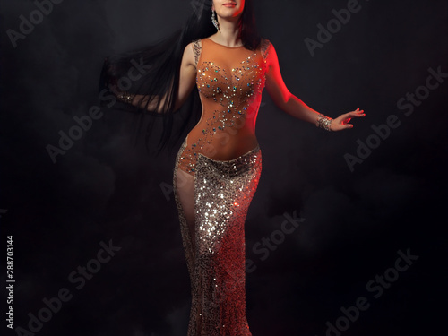 The body of a beautiful girl in a bead costume for belly dance on a black background of a stormy sky. Sexy dramatic woman dancing oriental dance in the light of red spotlights. photo