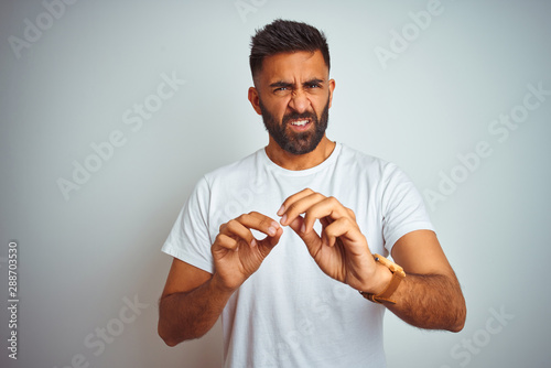 Young indian man wearing t-shirt standing over isolated white background disgusted expression, displeased and fearful doing disgust face because aversion reaction. With hands raised. Annoying concept.