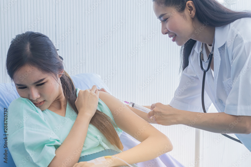 female doctor is injecting the woman patient with an expression of anxiety and lying in the hospital bed. Health care concept female doctor is injecting the woman patient with an expression of anxiety and lying in the hospital bed. Health care concept