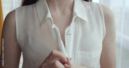 Unrecognizable woman unbuttoning white blouse at home.