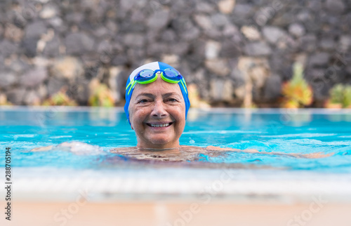 Happy senior active woman doing sport in the swimming pool. Outdoor under the sunlight. With swimming cap and goggles. Healthy lifestyle