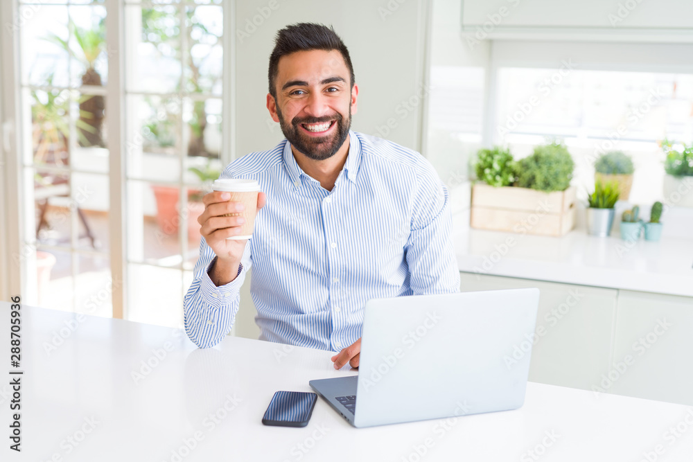 Handsome hispanic man working using computer laptop and drinking a cup of coffee with a happy face standing and smiling with a confident smile showing teeth Handsome hispanic man working using computer laptop and drinking a cup of coffee with a happy face standing and smiling with a confident smile showing teeth