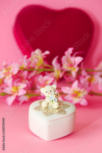 ceramic white casket with a teddy bear on a background of pink flowers and hearts