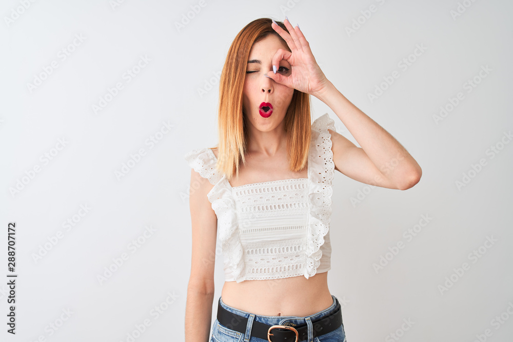 Beautiful redhead woman wearing casual t-shirt standing over isolated white background doing ok gesture shocked with surprised face, eye looking through fingers. Unbelieving expression. Beautiful redhead woman wearing casual t-shirt standing over isolated white background doing ok gesture shocked with surprised face, eye looking through fingers. Unbelieving expression.