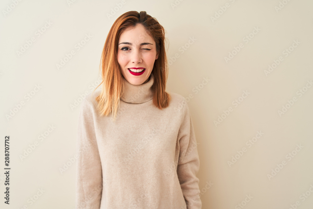 Redhead woman wearing elegant turtleneck sweater standing over isolated white background winking looking at the camera with sexy expression, cheerful and happy face. Redhead woman wearing elegant turtleneck sweater standing over isolated white background winking looking at the camera with sexy expression, cheerful and happy face.