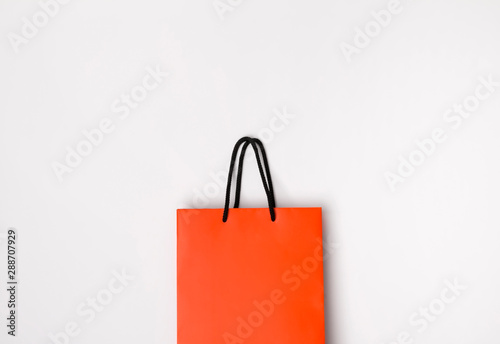 Orange paper shopping bag with black handles on the white background